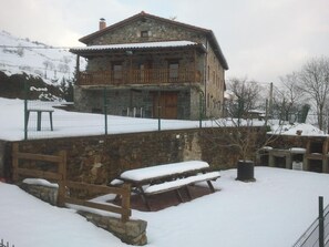 Un edificio de piedra con balcón, rodeado de nieve y una cerca.