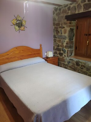 Un dormitorio con cama de madera, pared de piedra y armario de madera.
