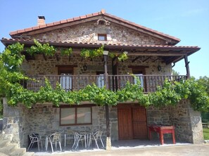 Un edificio de piedra con balcón, una puerta de madera y asientos al aire libre.