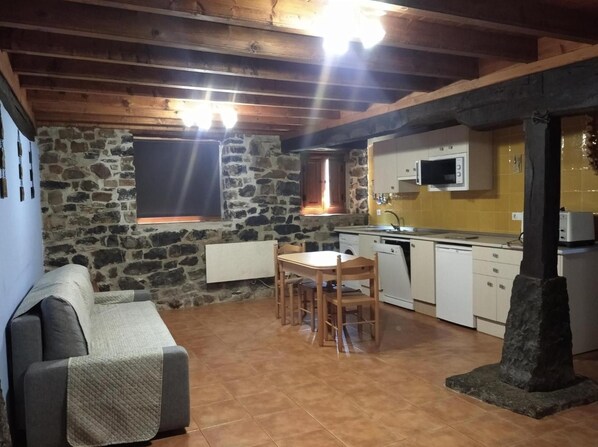 Una cocina rústica con paredes de piedra, una mesa de comedor con sillas, un microondas integrado y una chimenea de piedra.