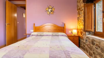 Une chambre avec un lit en bois, une table de chevet avec une lampe, un mur en pierre et une porte.