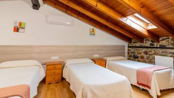Una habitación con tres camas, pisos de madera, una pared de piedra y un techo inclinado con vigas de madera.