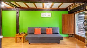 Une pièce avec un canapé gris, deux coussins orange, une petite table en bois ornée d’un objet décoratif et un mur vert.