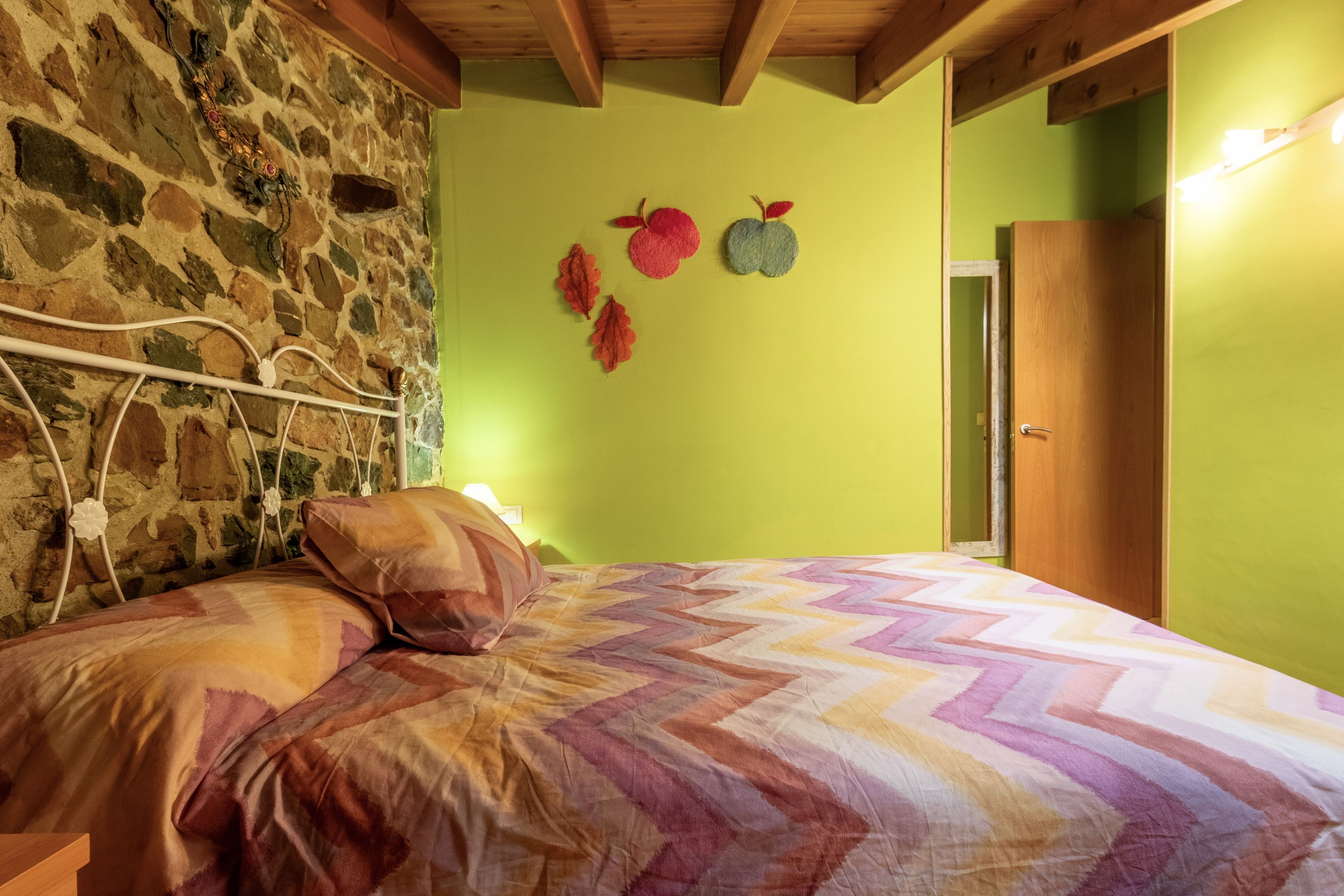 A room with a bed, a stone wall, and a green wall with leaf decorations.