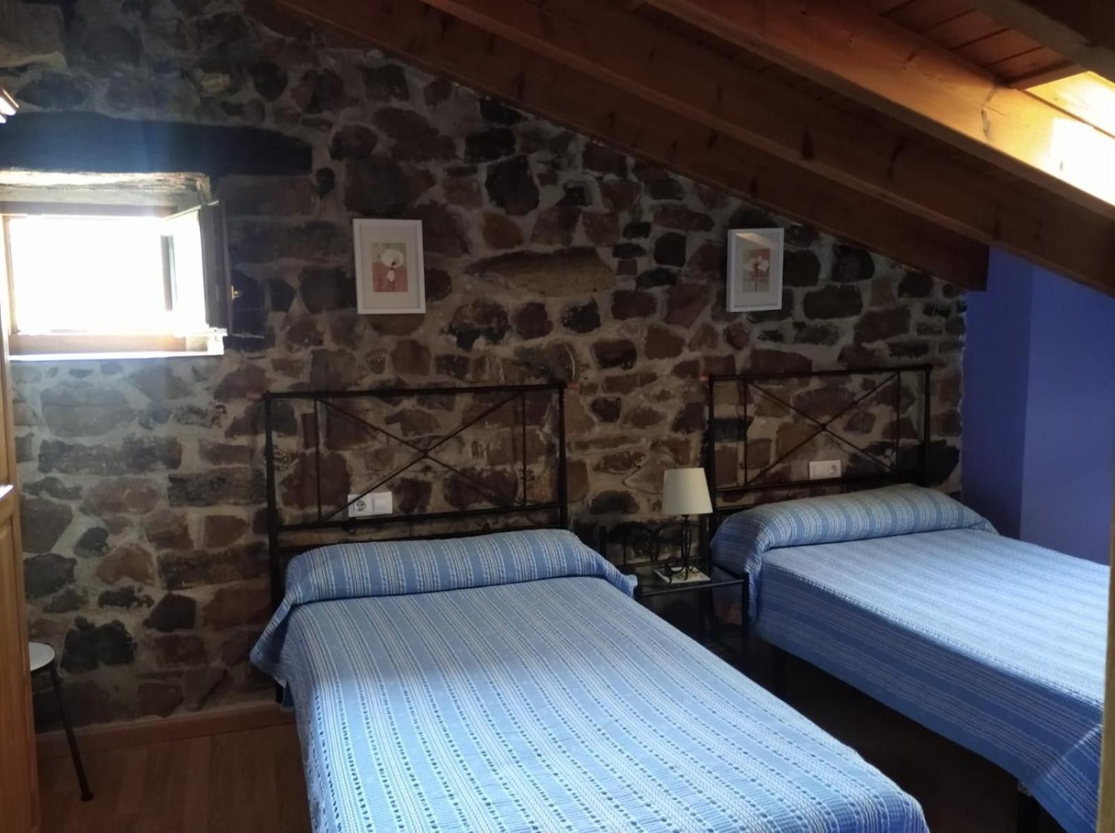 Una habitación con dos camas, paredes de piedra, techo de madera y una ventana.