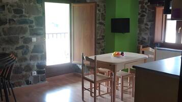 Una habitación con pared de piedra, una mesa de madera con sillas, una pared verde decorativa y un televisor montado en la pared.
