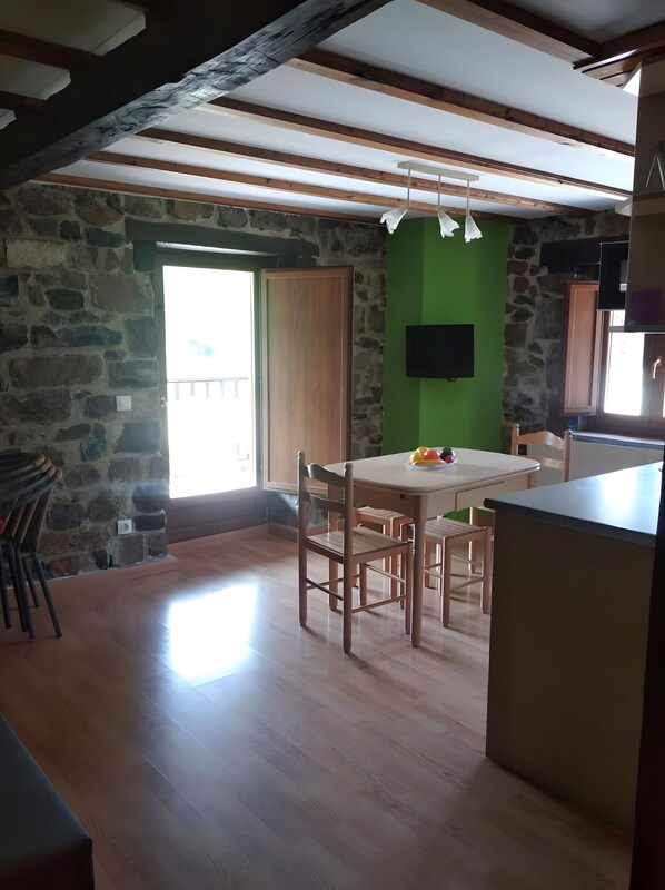 Una habitación con pared de piedra, una mesa de madera con sillas, una pared verde decorativa y un televisor montado en la pared.