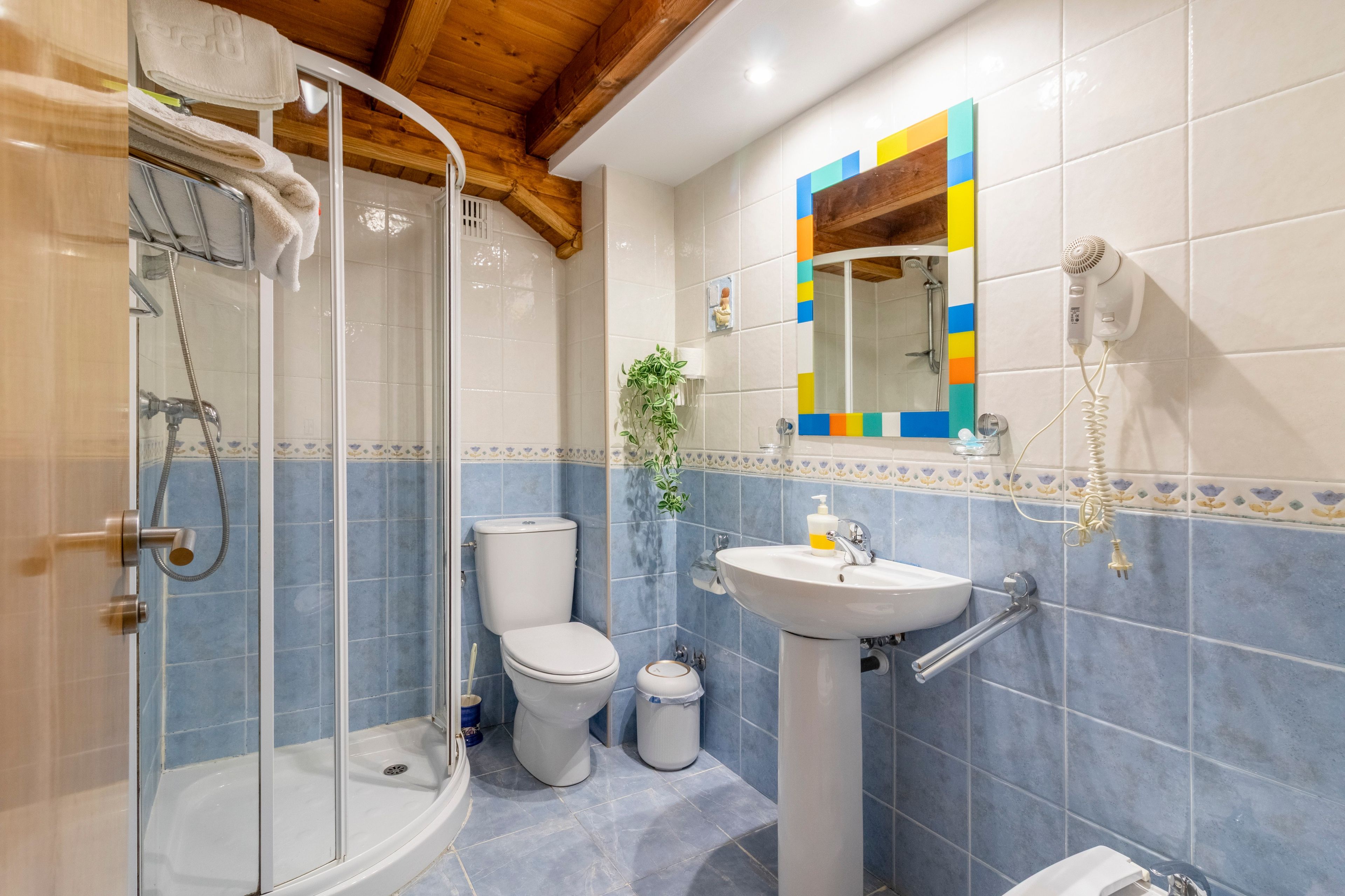 Un baño con ducha, inodoro, lavamanos y espejo con un marco colorido.