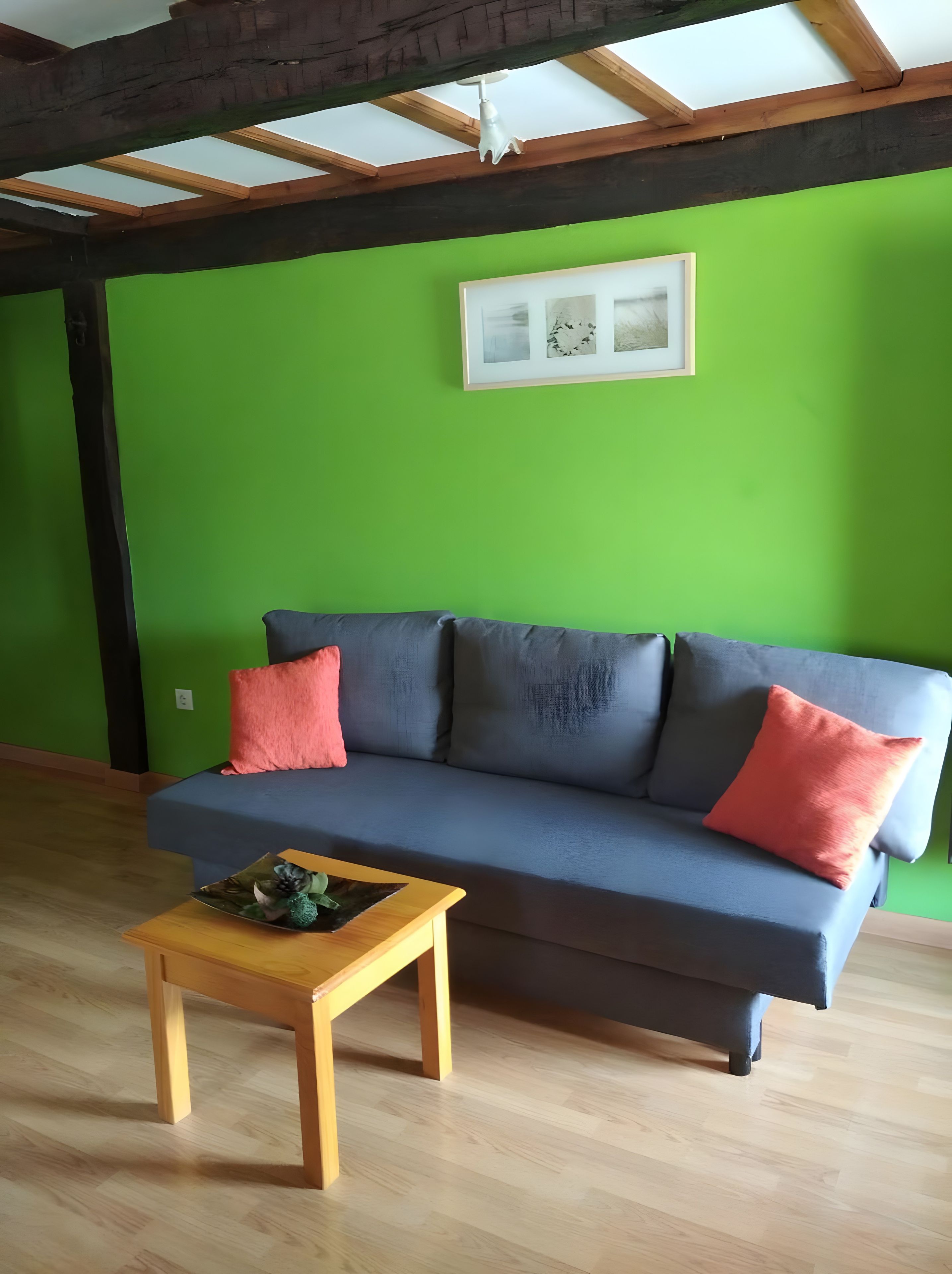 A room with a green wall, a grey sofa with red cushions, and a wooden coffee table.