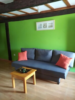 A room with a green wall, a grey sofa with red cushions, and a wooden coffee table.