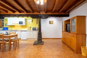 A kitchen with wooden beams, a dining table, chairs, a stone pillar, and a TV cabinet. - Apartment 'El Valle De Soba' with Shared Garden and Wi-Fi (La Barcenilla)