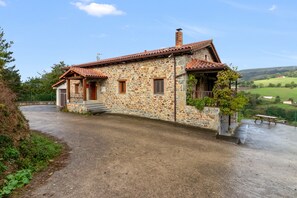Une maison en pierre avec un toit en tuiles, un porche à l’avant et une vue sur la campagne.
