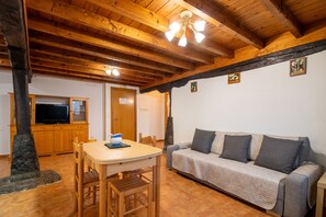 A cozy room with a wooden ceiling, a sofa, a table with chairs, and a television. - Apartment 'El Valle De Soba' with Shared Garden and Wi-Fi (La Barcenilla)