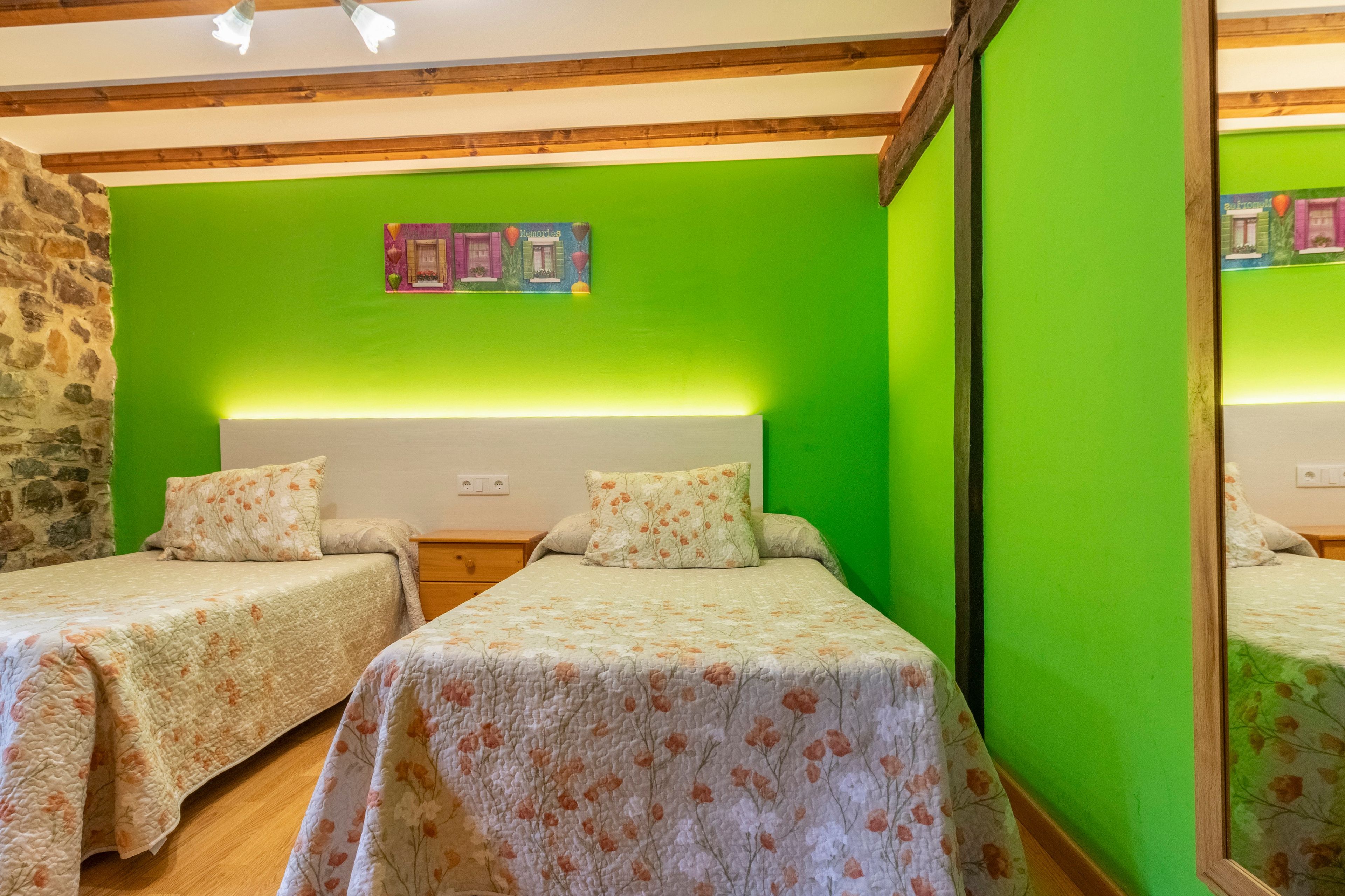 Una habitación con dos camas, una pared de piedra y una pared verde con un cuadro enmarcado.
