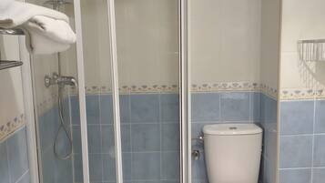 Un baño con cabina de ducha de vidrio, inodoro y paredes con azulejos azules.