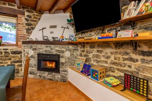 A cozy living room with a stone fireplace, a television, and various children's toys and books on shelves.