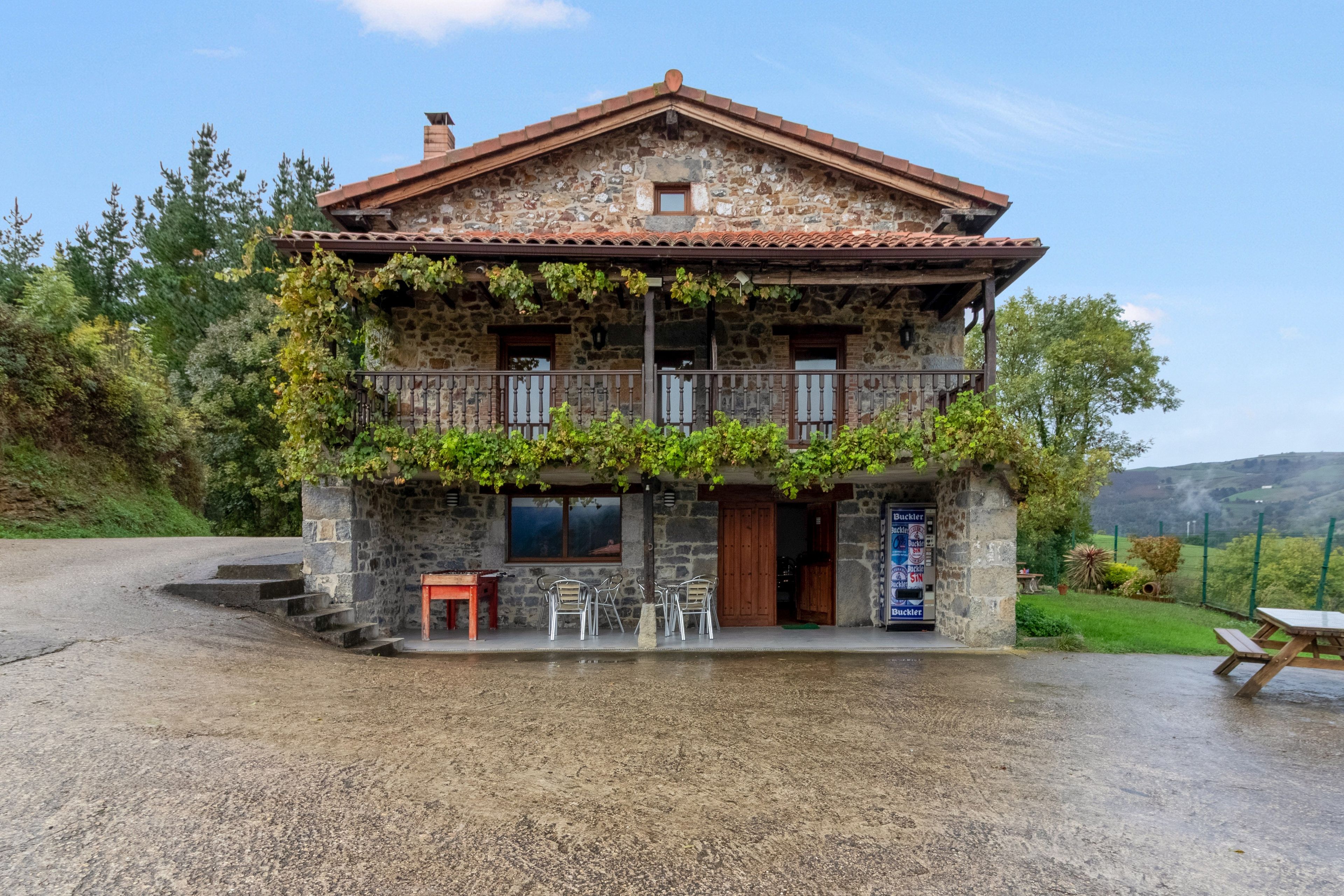 Un edificio de piedra de dos pisos con balcón, asientos exteriores y vistas del paisaje circundante.
