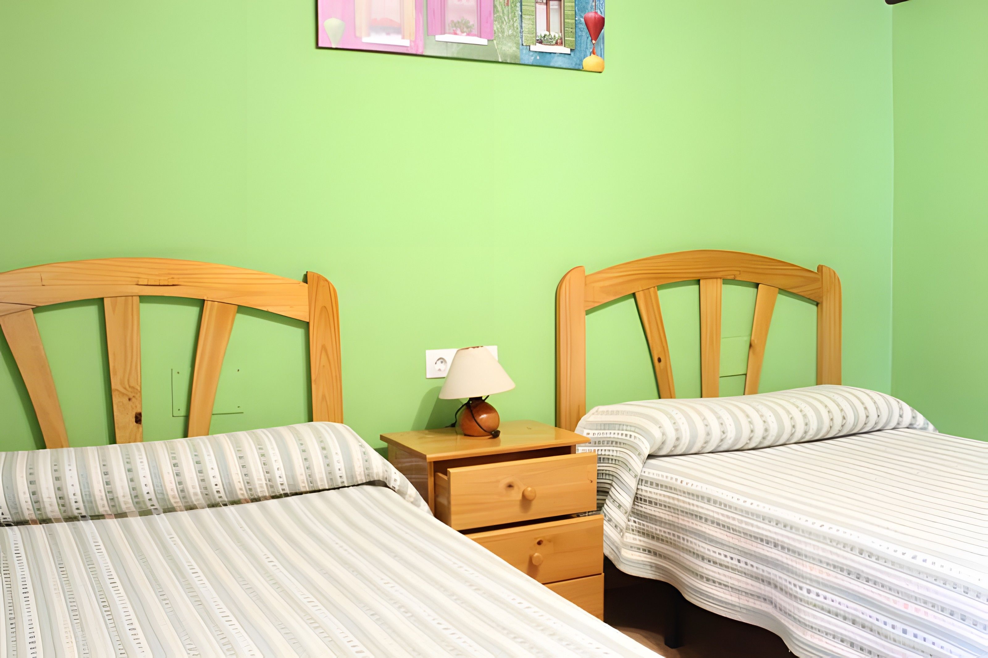Una habitación con dos camas de madera, una mesita de noche con lámpara y un enchufe en la pared.