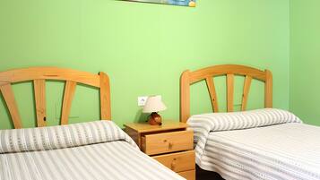 Una habitación con dos camas de madera, una mesita de noche con lámpara y un enchufe en la pared.