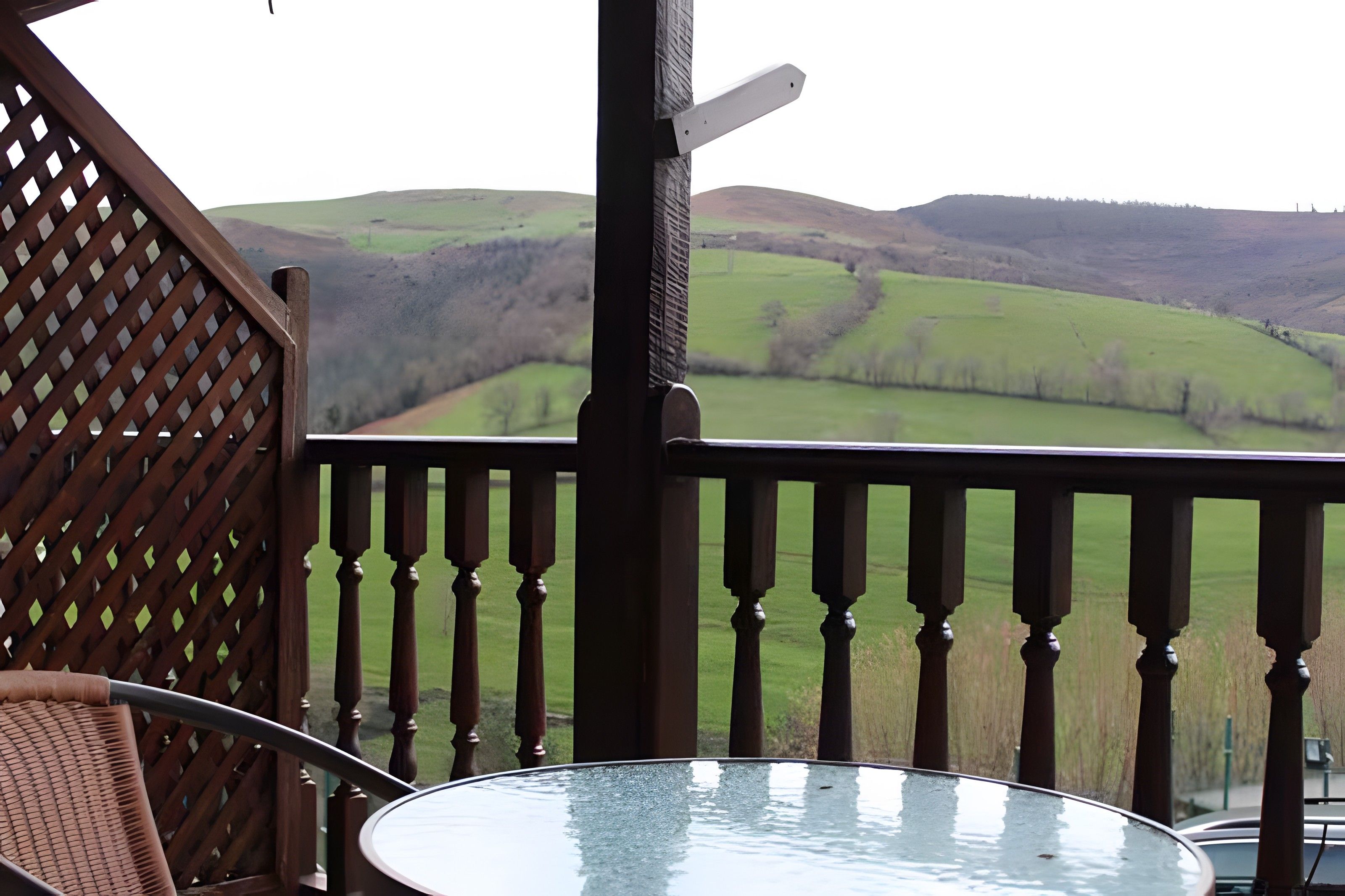 A balcony with a glass table and a view of rolling hills.