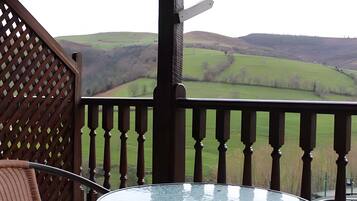 A balcony with a glass table and a view of rolling hills.