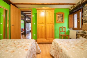 A room with two beds, wooden wardrobe, stone wall, and a chair.