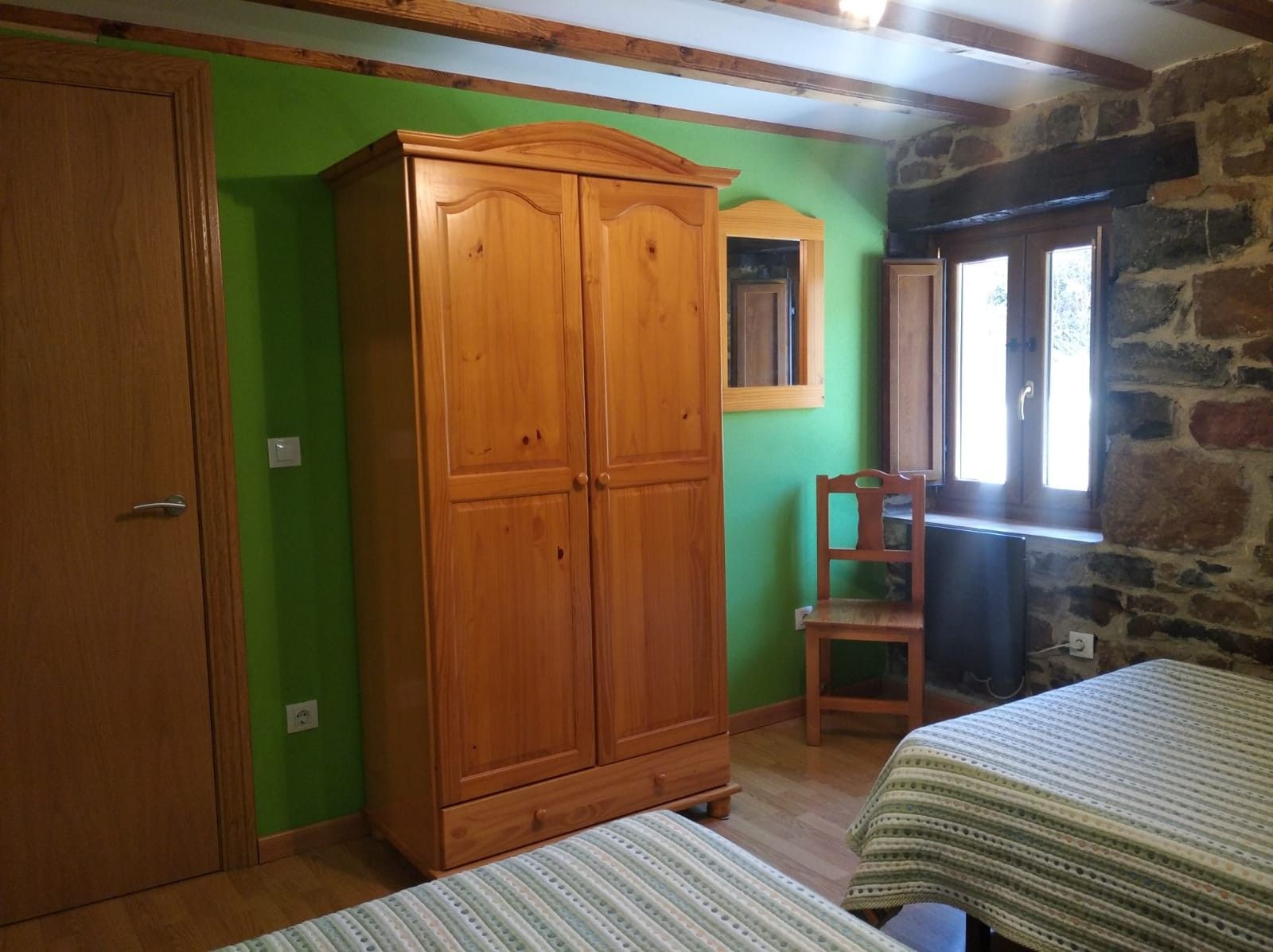 Una habitación con un armario de madera, una silla y dos camas con ropa de cama a rayas.