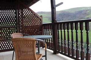 Ein überdachter Außenbereich mit Tisch und Stühlen, der auf eine hügelige Landschaft blickt.