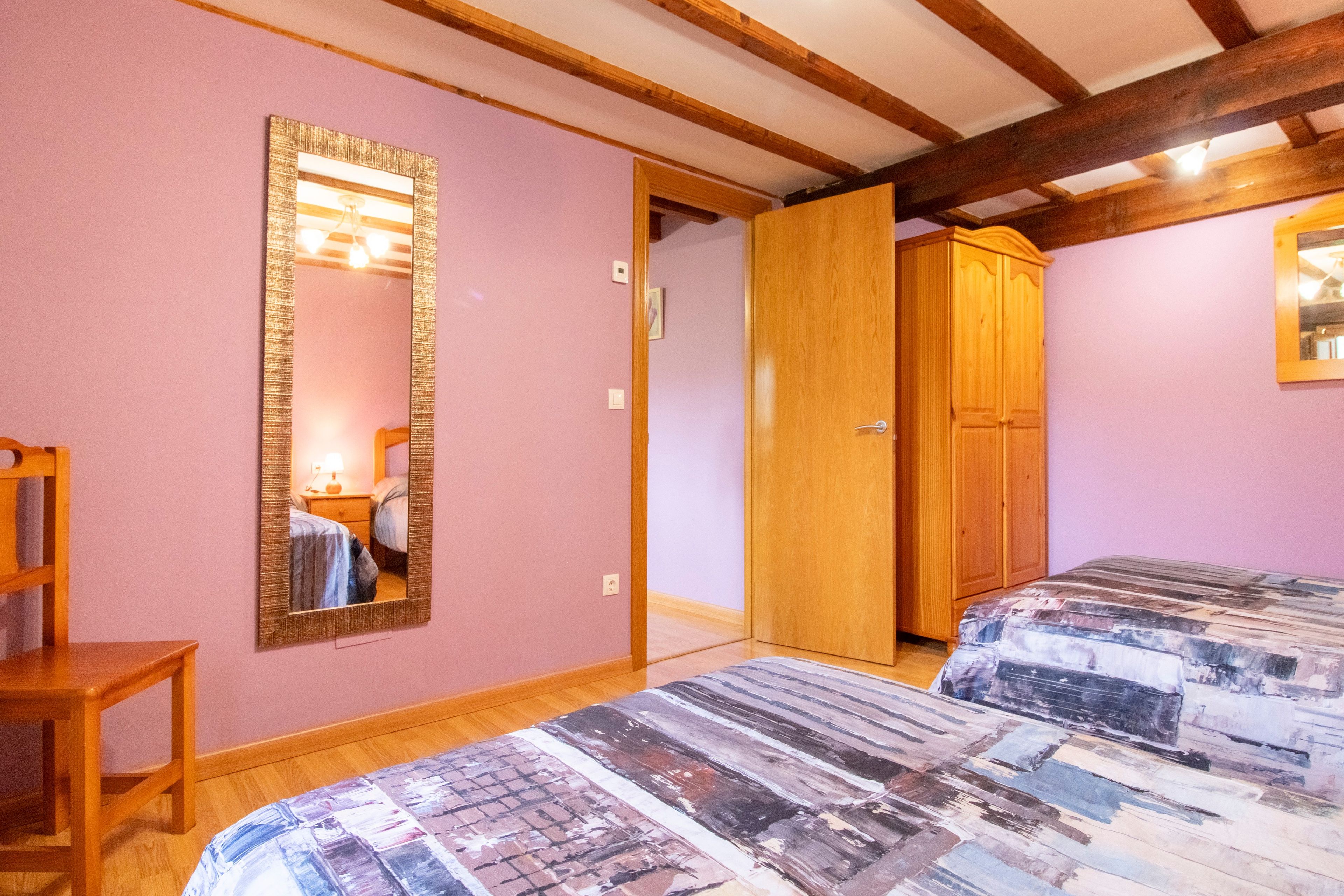 Une chambre avec deux lits, une armoire en bois, un miroir et une chaise en bois.