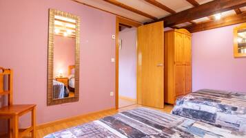 Une chambre avec deux lits, une armoire en bois, un miroir et une chaise en bois.