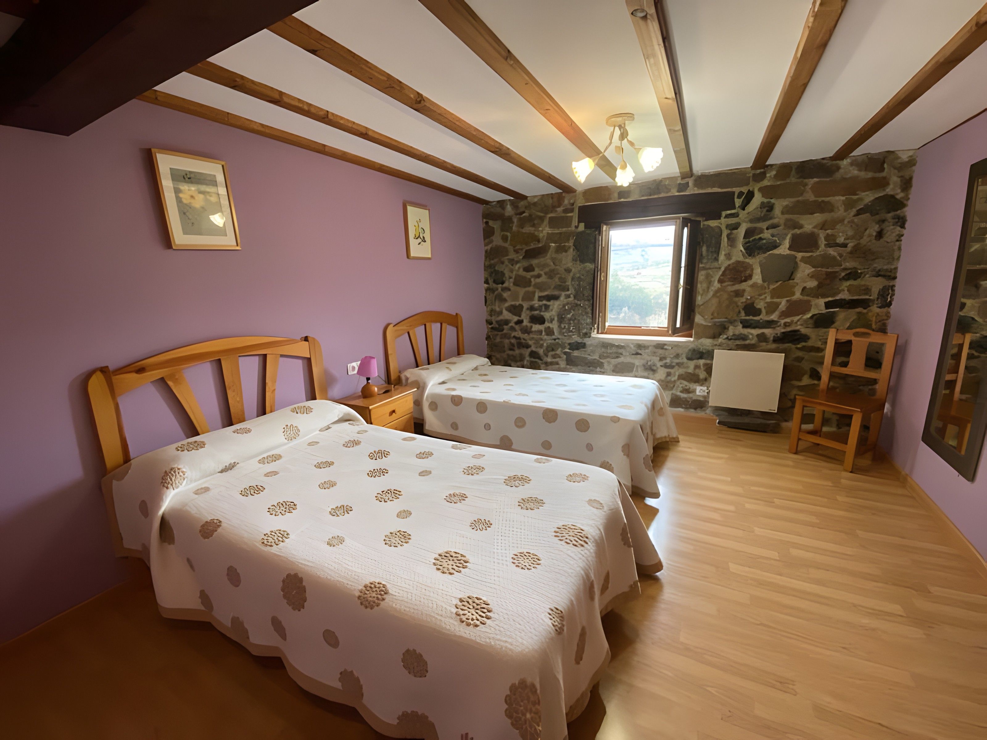 Een kamer met twee bedden, een stenen muur, een raam en een houten plafond.