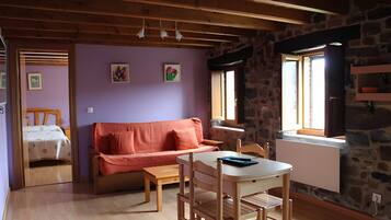 Een gezellige kamer met een houten plafond, een stenen muur, een paarse muur, een houten tafel met stoelen, een bank en een bed met stippenbeddels.