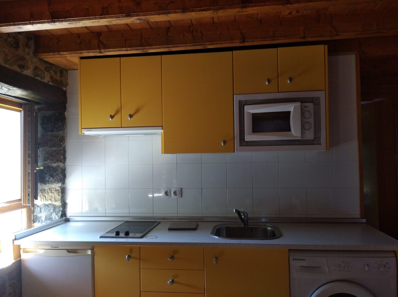 Cocina compacta con armarios amarillos, microondas integrado, fregadero y lavavajillas.
