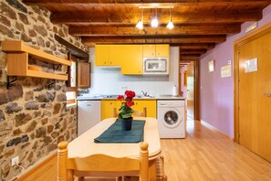 A compact kitchen with a stone wall, wooden beams, a table with a green tablecloth, and a washing machine.