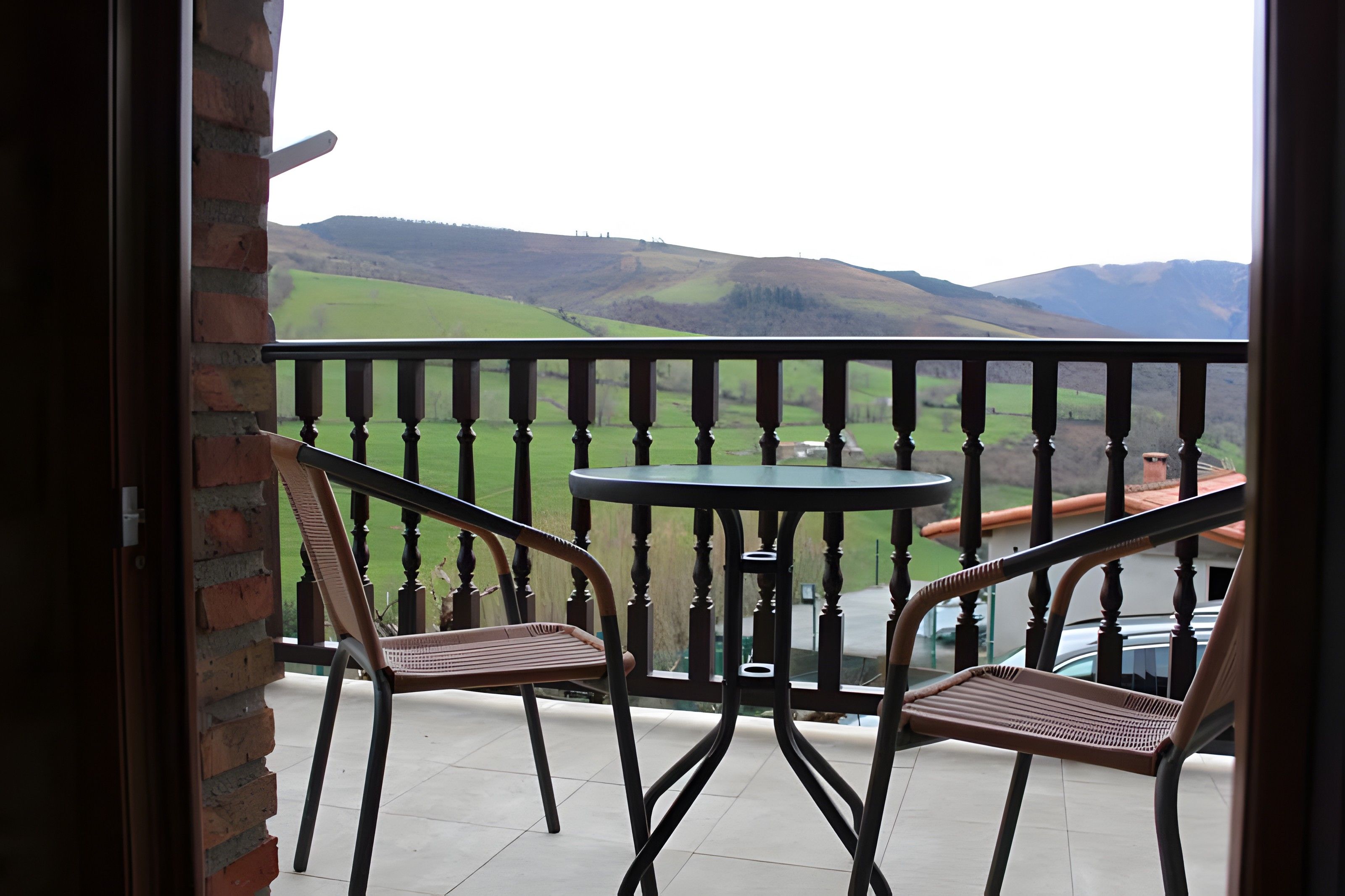 Un balcón con dos sillas y una mesa, con vistas a un paisaje verde con colinas.
