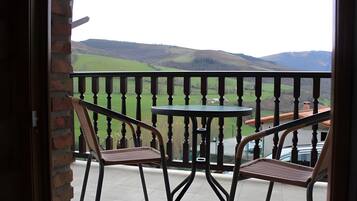Un balcón con dos sillas y una mesa, con vistas a un paisaje verde con colinas.