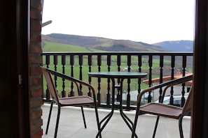 Un balcón con dos sillas y una mesa, con vistas a un paisaje verde con colinas.