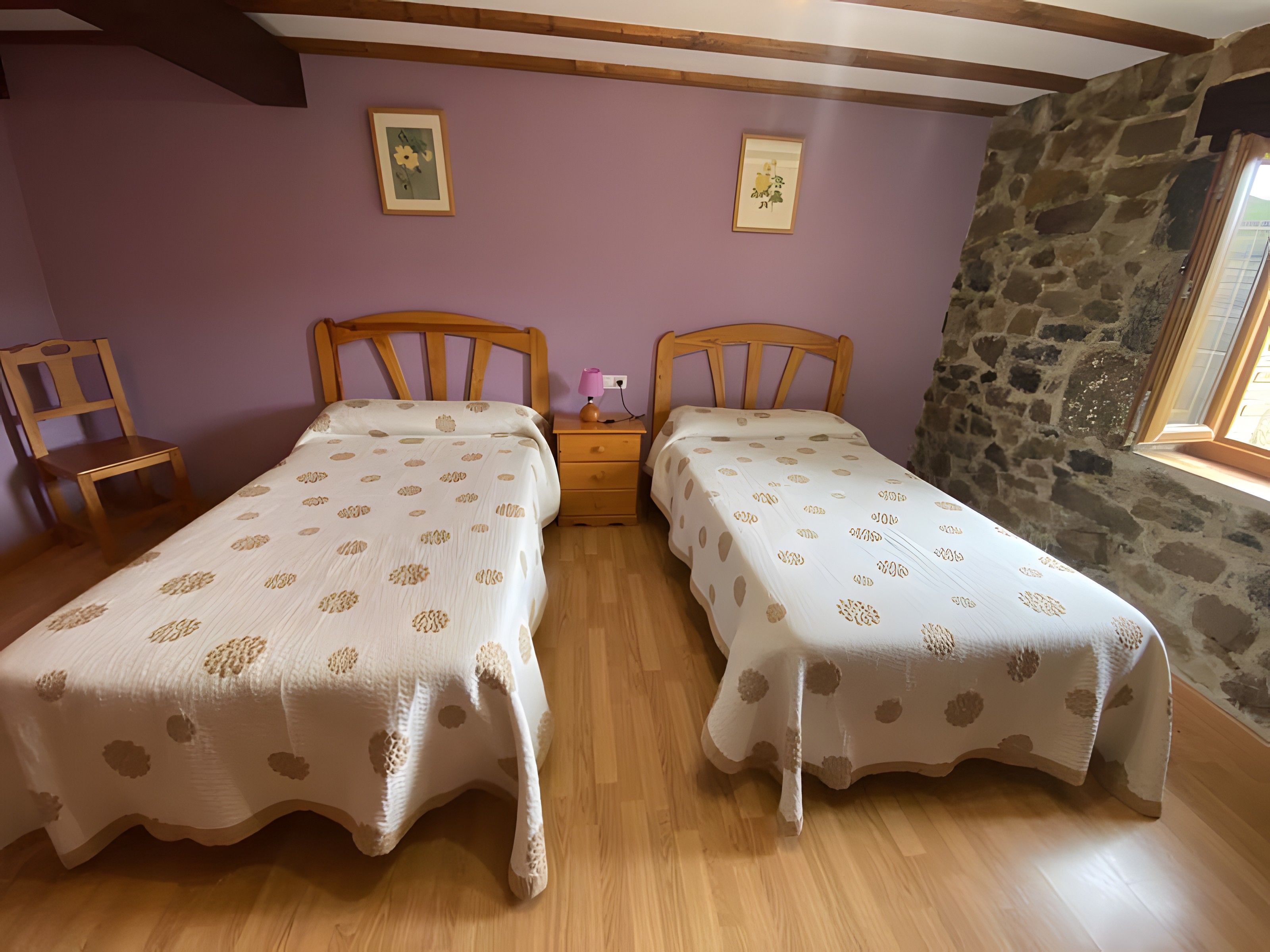 Een slaapkamer met twee eenpersoonsbedden, houten hoofdborden, een nachtkastje met een lamp en een stenen muur.