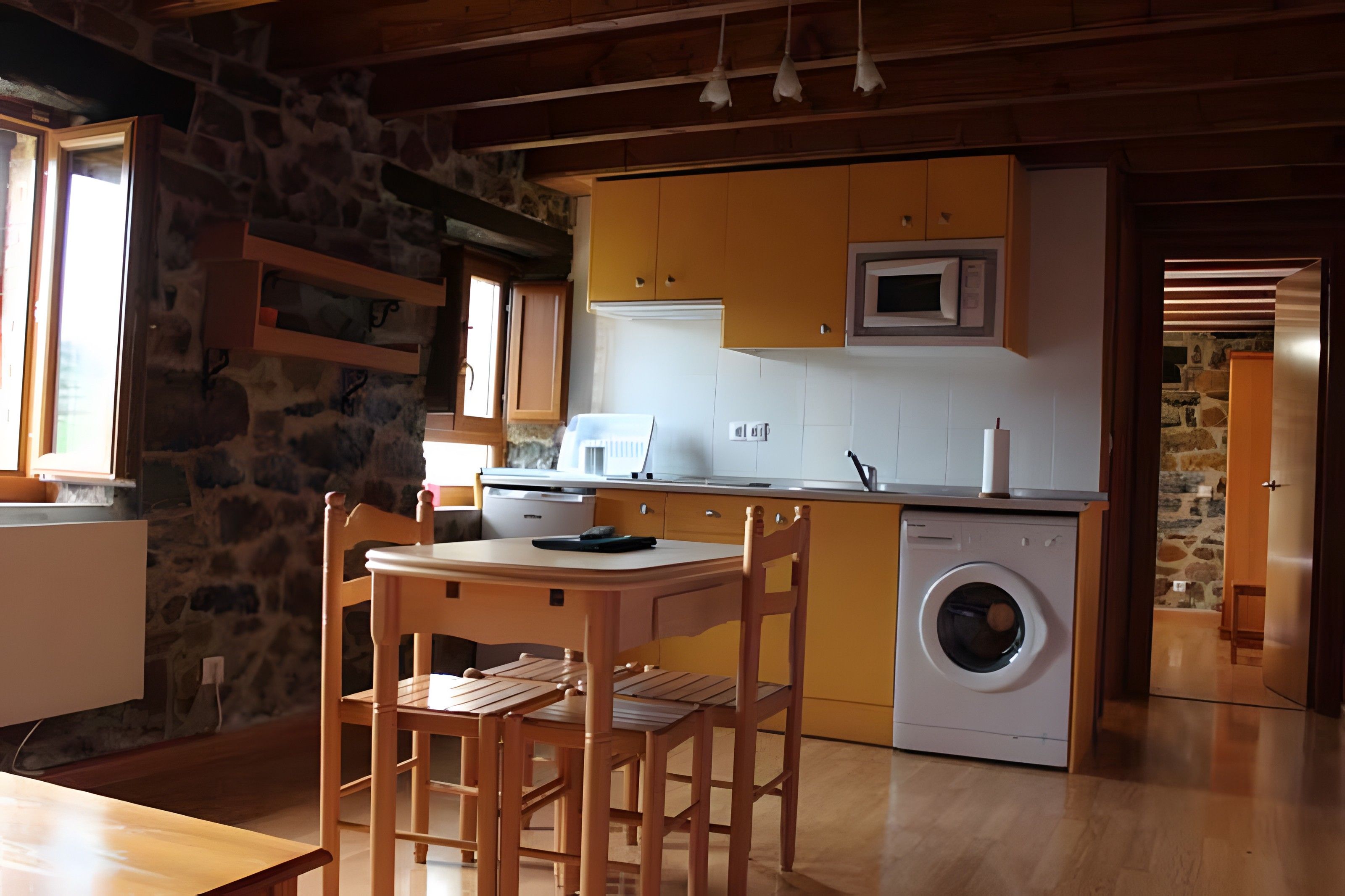 Une cuisine de taille réduite équipée d’un lave-linge, d’une table à manger en bois et de chaises.