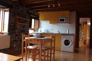Een kleine keuken met een wasmachine, een houten eettafel en stoelen.