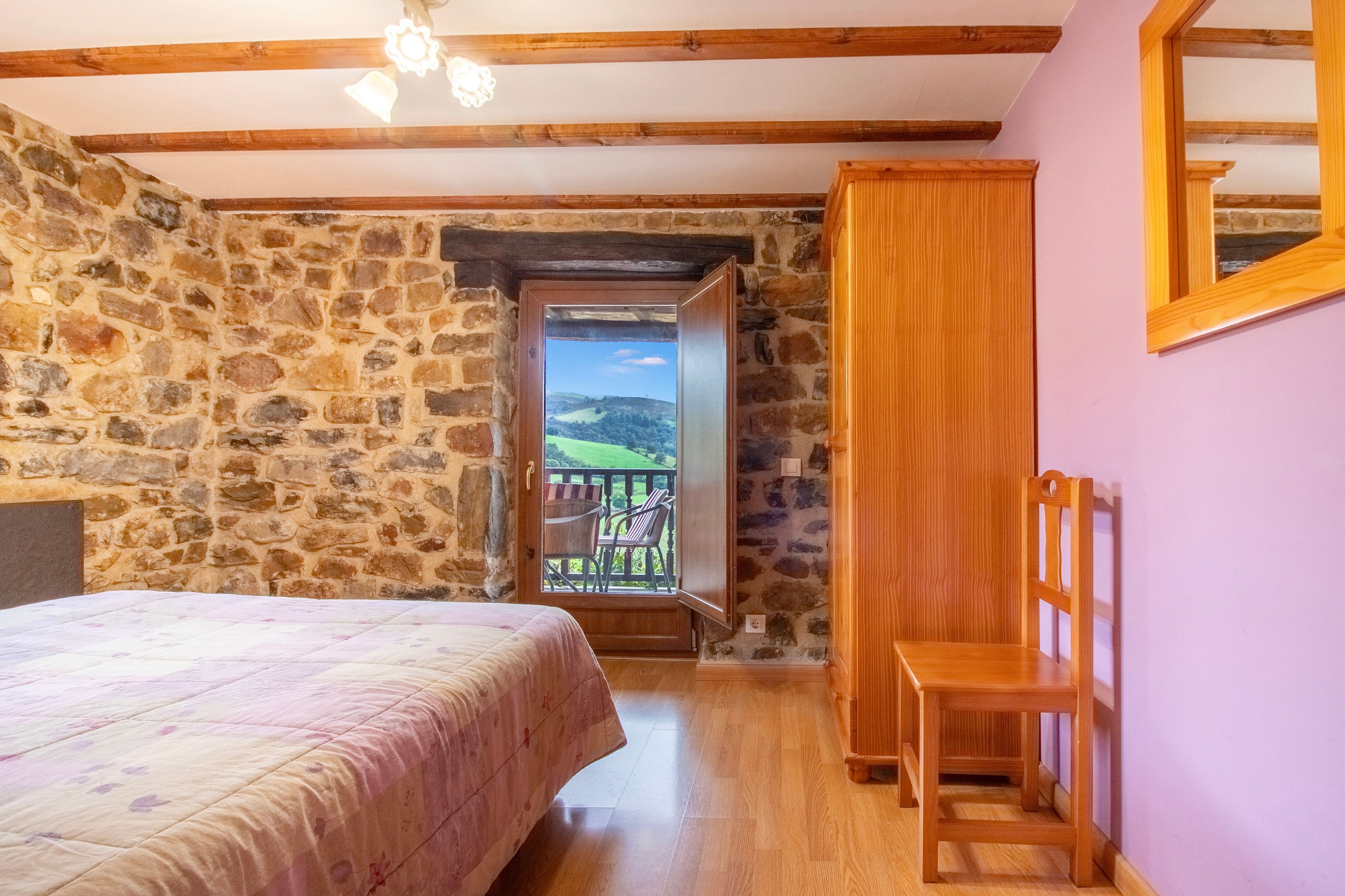 Un dormitorio con pared de piedra, cama de madera, silla de madera y un balcón con vistas.