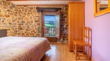 Un dormitorio con pared de piedra, cama de madera, silla de madera y un balcón con vistas.