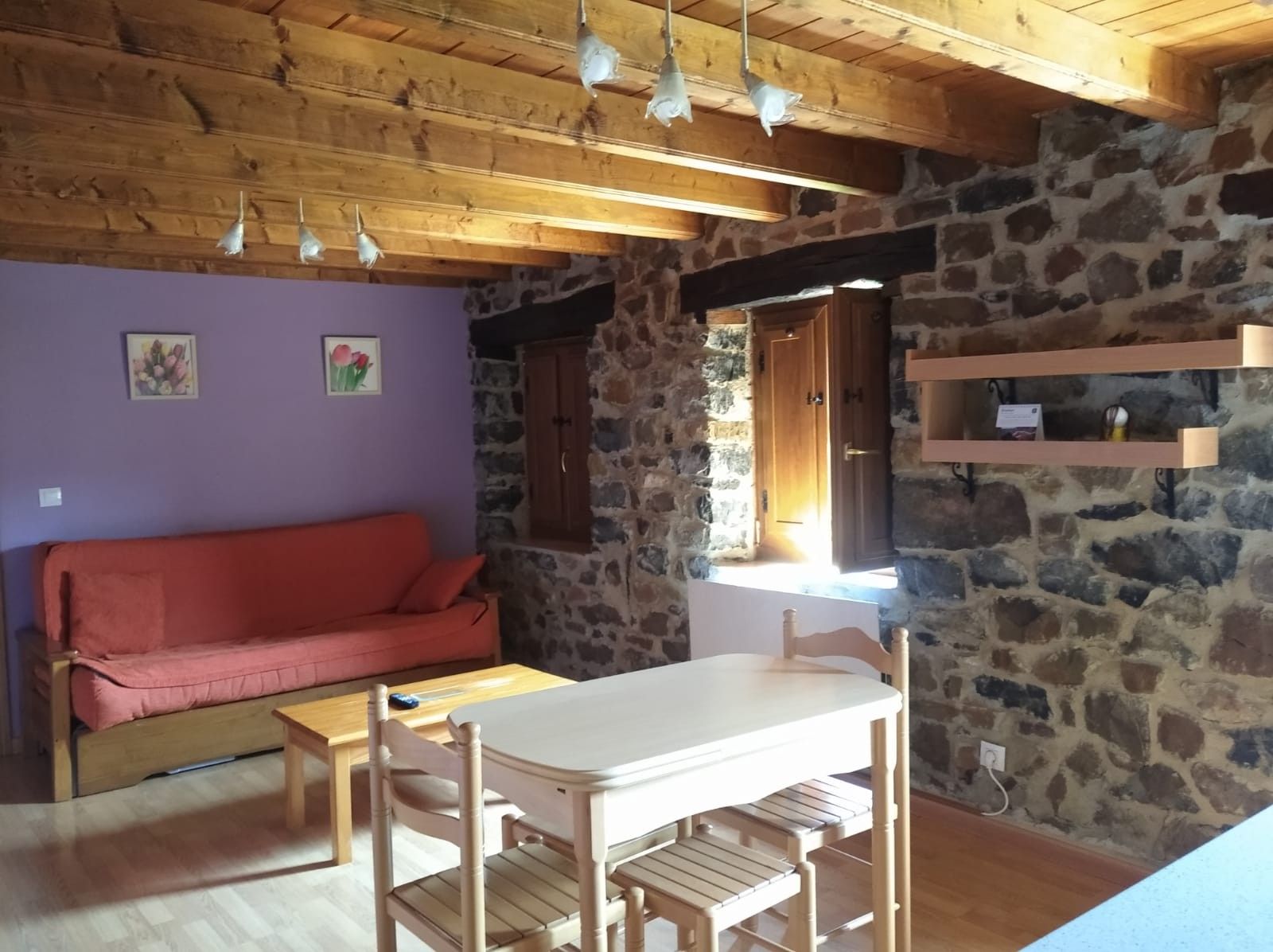 Une pièce chaleureuse avec un plafond en bois, des murs en pierre, un canapé rouge, une table en bois et une fenêtre donnant sur un beau paysage.