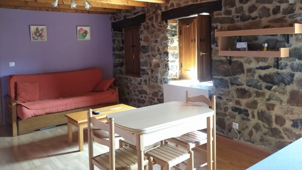 Una habitación acogedora con techo de madera, paredes de piedra, un sofá rojo, una mesa de madera y una ventana con vistas.