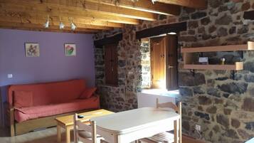Une pièce chaleureuse avec un plafond en bois, des murs en pierre, un canapé rouge, une table en bois et une fenêtre donnant sur un beau paysage.