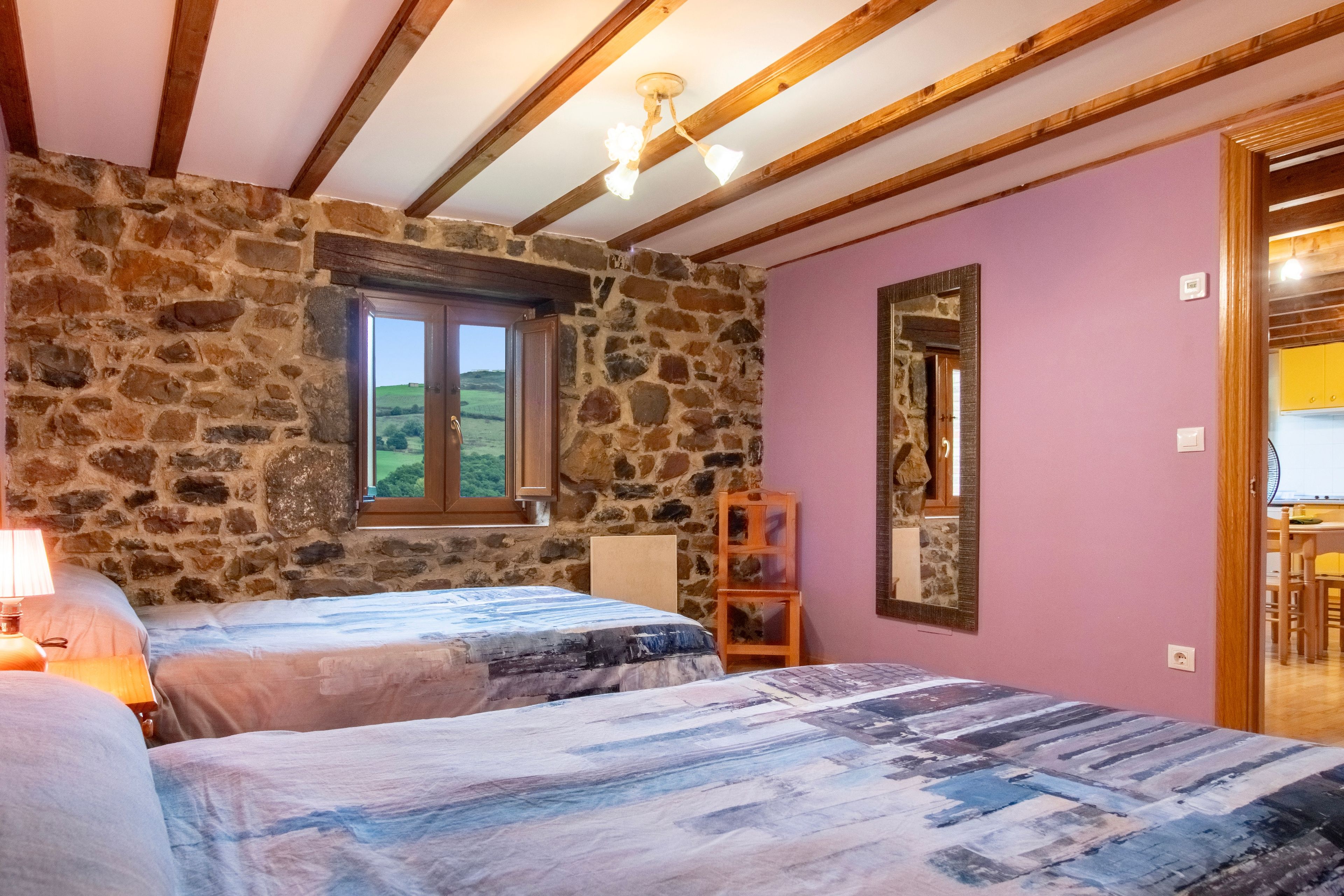 Een slaapkamer met twee bedden, een stenen muur, een raam en een spiegel.