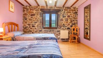 Une chambre avec un mur en pierre, un lit en bois, une fenêtre, une chaise et une lampe.