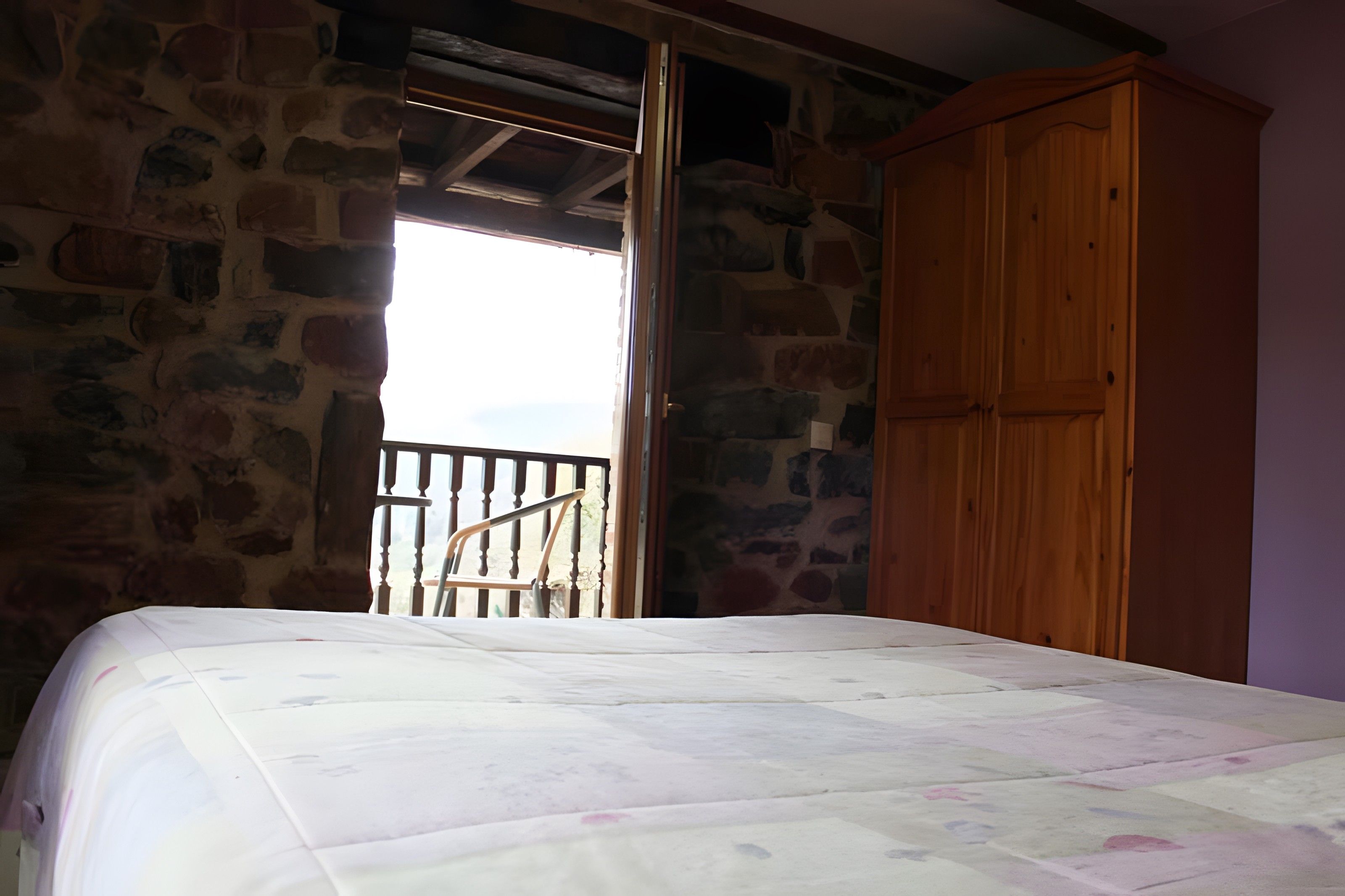 Une chambre à coucher avec un lit, une armoire en bois et un mur en pierre.
