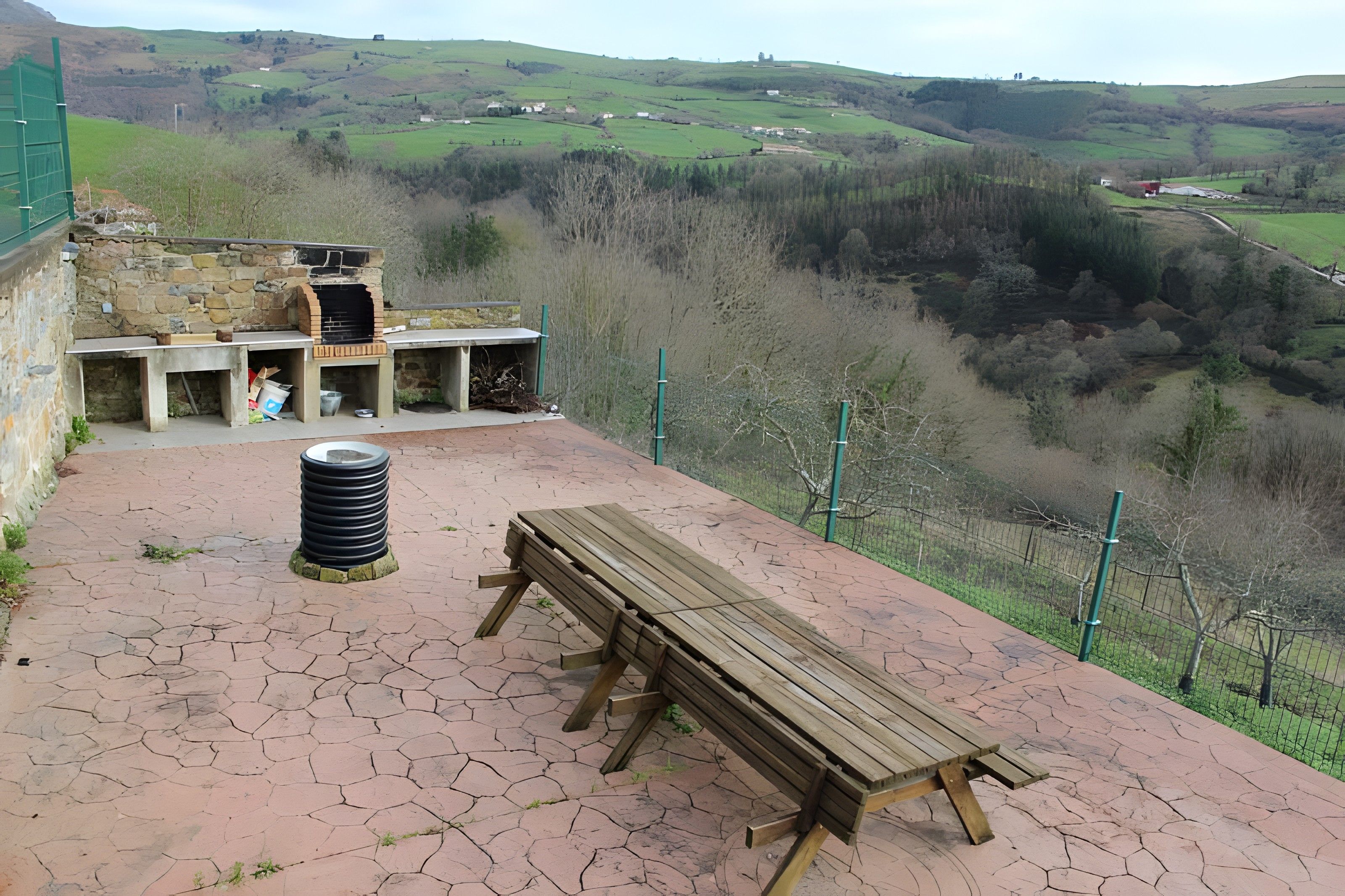 Un espace extérieur rustique aménagé avec un barbecue en pierre, un banc en bois et une table de pique-nique.