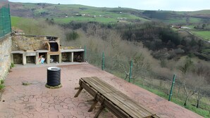 Un espacio al aire libre rústico con una parrilla de piedra, un banco de madera y una mesa de picnic.